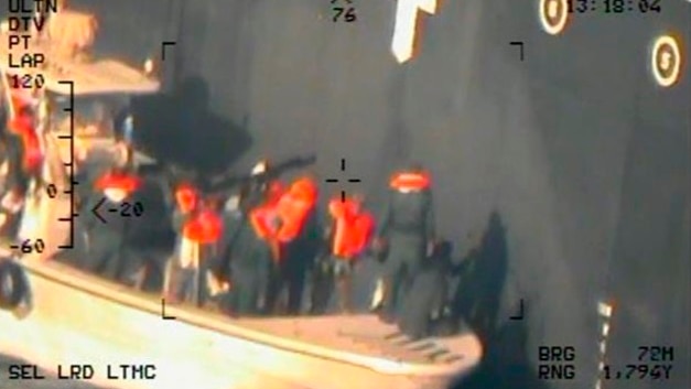 A blurred photo shows men standing on a boat beside a ship at sea