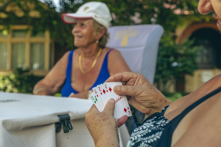 A woman holds her cards up, with her friends sitting around the same table in a park