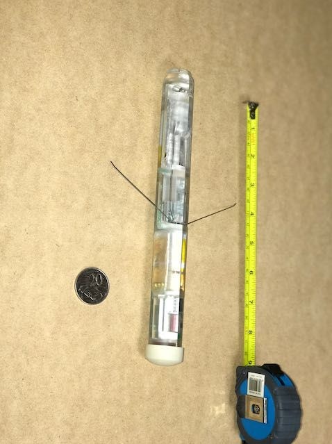 A cylindrical device sitting next to a 20 cent coin and tape measure for scale