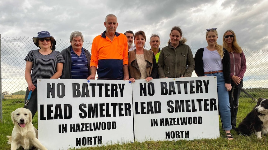 A group of community members stand outside the site of a proposed battery recycling centre with two signs