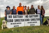 A group of community members stand outside the site of a proposed battery recycling centre with two signs.