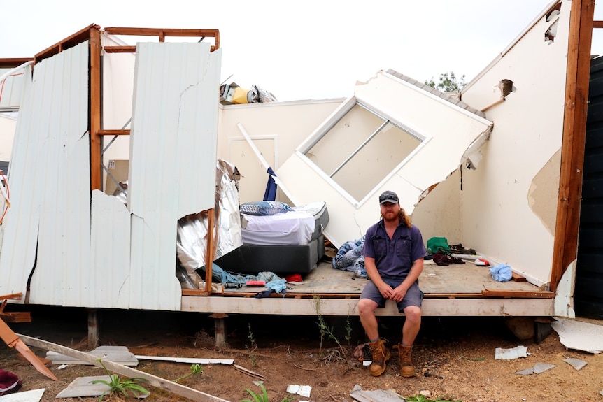 Man sitting on edge of open room with debris behind him.