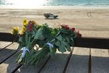 Flowers lay on a bench with a sprawling beach in the background