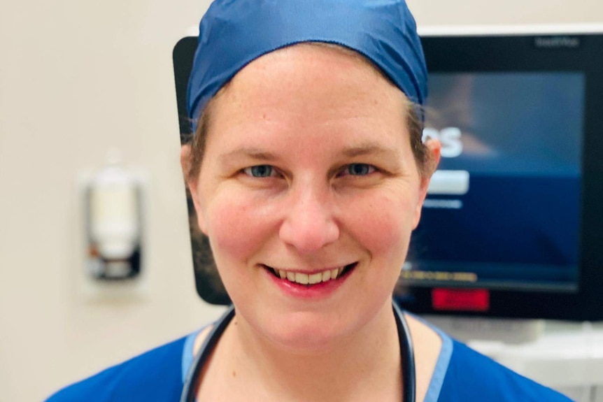 A close up of a woman in scrubs smiling at the camera