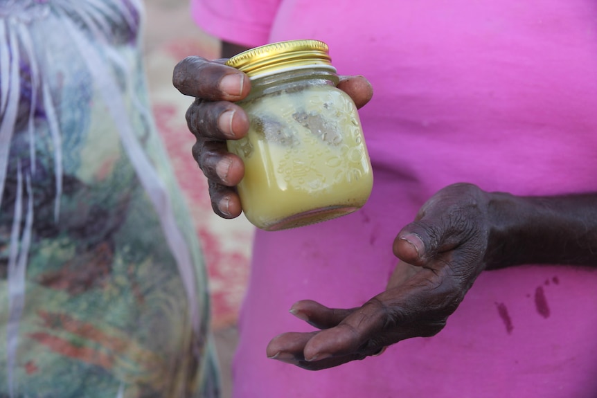 A hand holding a small jar with yellow cream.