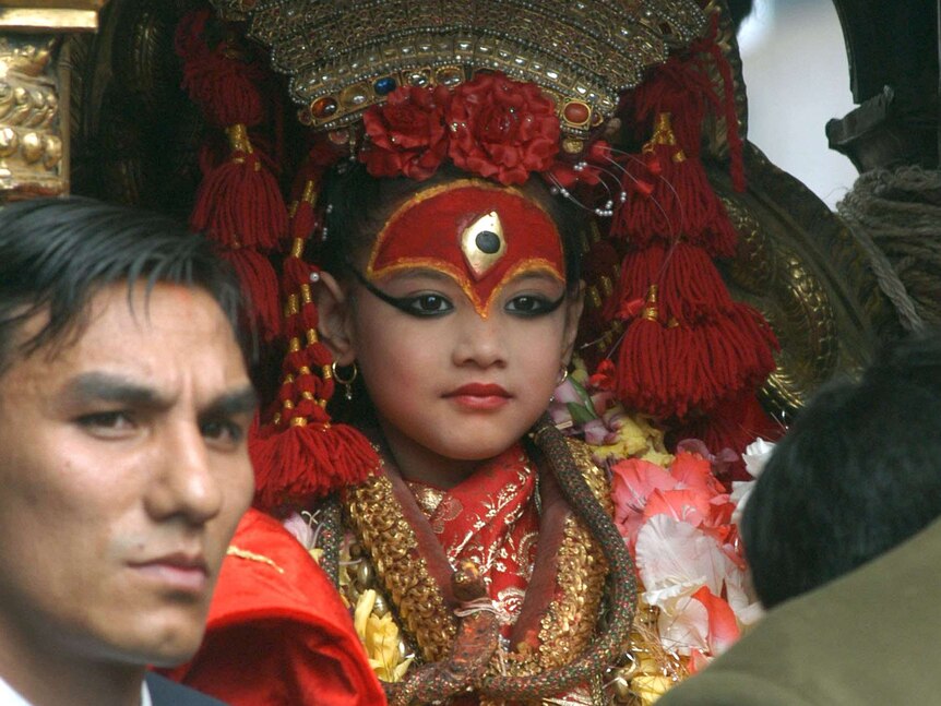 A devotee bows his head in front of the child goddess in ceremonial dress