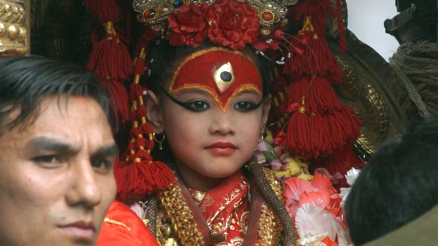 A devotee bows his head in front of the child goddess in ceremonial dress