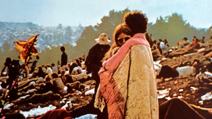 A couple embrace, surrounded by people sitting and lying on the ground, at Woodstock in 1970.