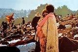 A couple embrace, surrounded by people sitting and lying on the ground, at Woodstock in 1970.