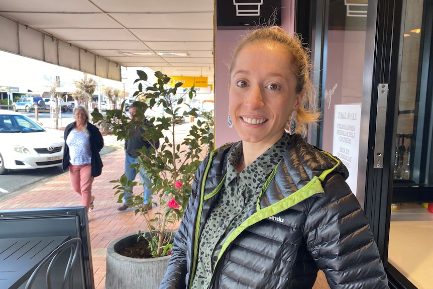 A woman on a footpath looking at the camera smiling.