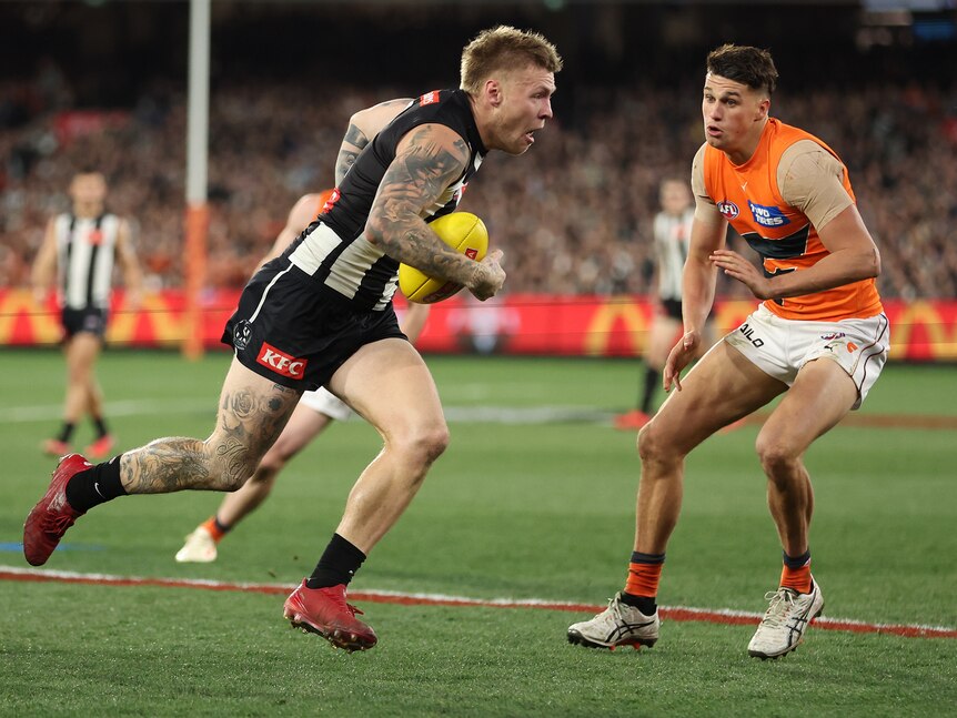 Collingwood's Jordan de Goey tucks the ball under his arm and runs past a GWS defender during a final.