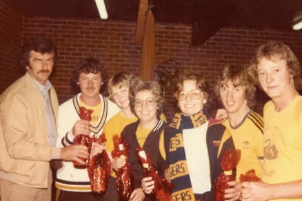 A group of people, some wearing football scarves, smile for the camera.