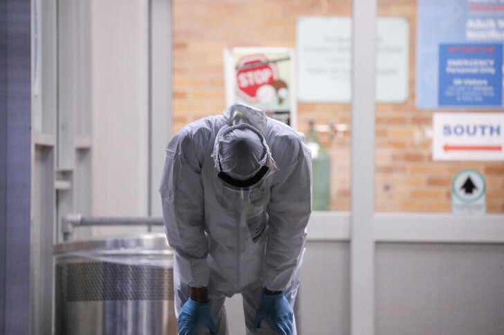 A man in full protective gear puts his head down and his hands on his thighs