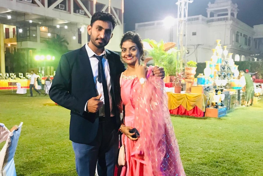 A young Indian couple smiling in a suit and pink sari.