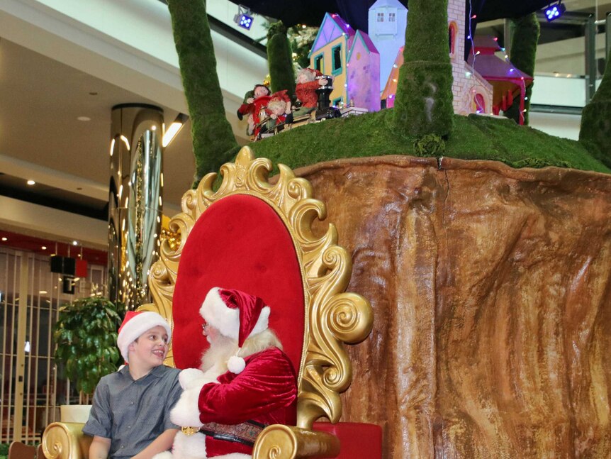 Diego Marraffa sits in Santa's chair and smiles at him in a shopping centre