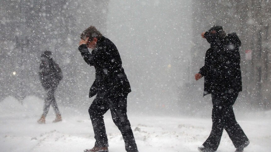 Two men hold their hands over their eyes as they struggle to walk through a snowstorm in Boston.