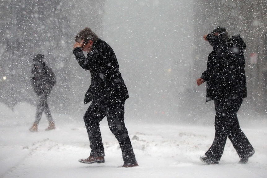 Two men hold their hands over their eyes as they struggle to walk through a snowstorm in Boston.