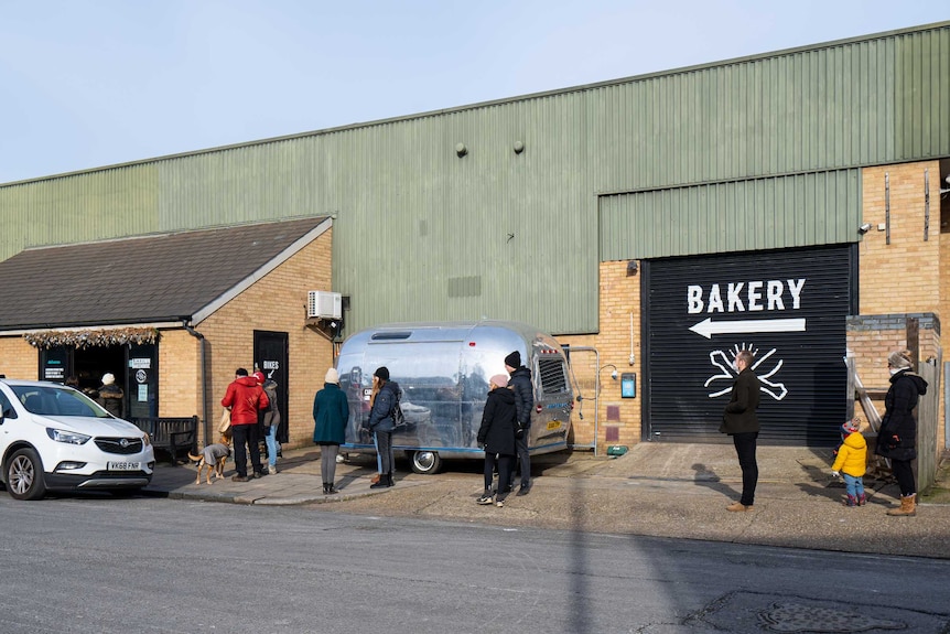 Customers stand in a socially-distanced line outside of a bakery in an industrial area of London.