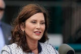 Michigan Governor Gretchen Whitmer is standing at a microphone, wearing red lipstick. 