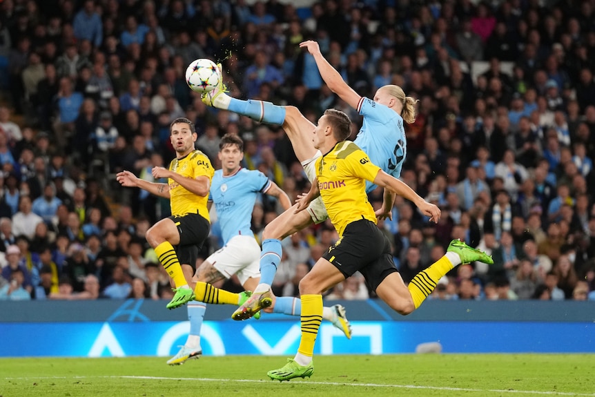 Erling Haaland of Manchester City leaps and kicks the ball in mid-air while Borussia Dortmund defenders chase.