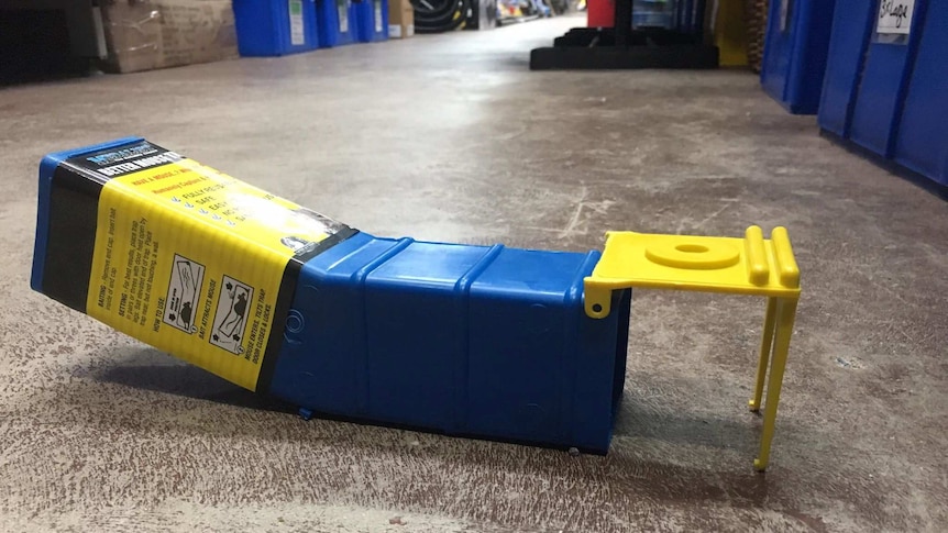 A blue and yellow box that tilts up at one end and has a hole at the other end on the floor of a hardware store