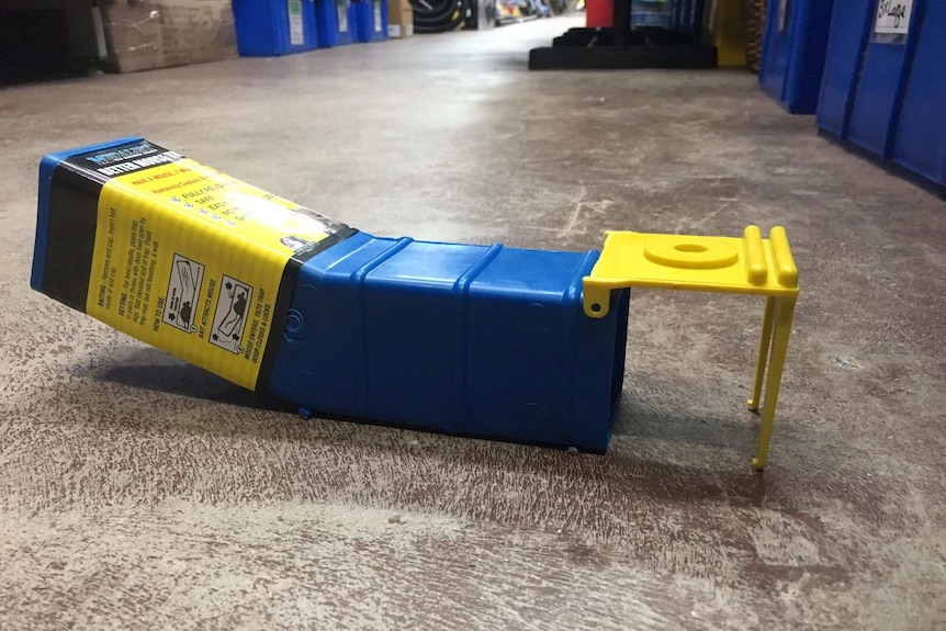 A blue and yellow box that tilts up at one end and has a hole at the other end on the floor of a hardware store