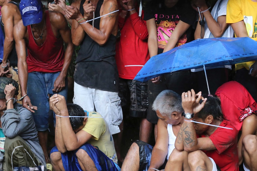 Police restrain men from poor Philippines community in drugs crackdown.