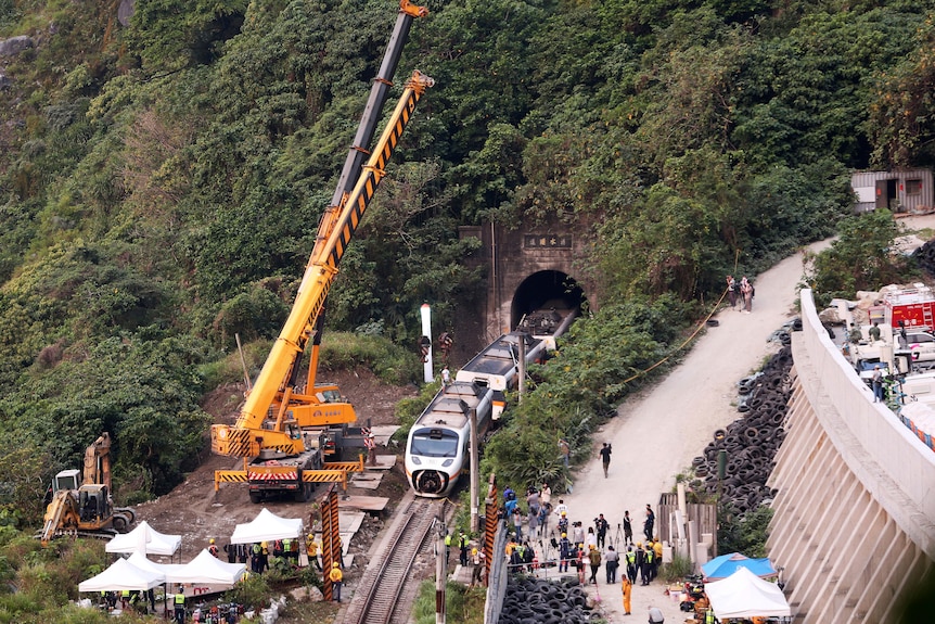 An aerial shot of a large crane looming over a staionary train emerging from a tunnel.