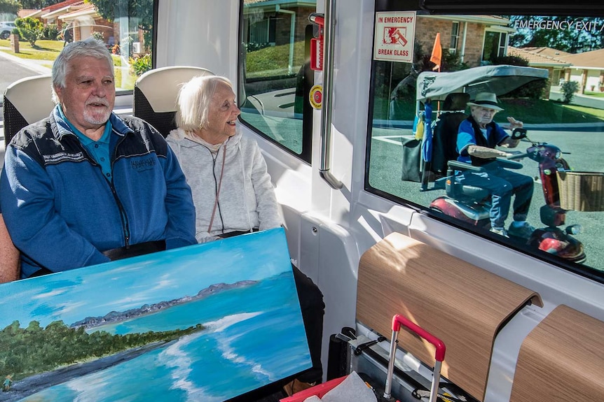 Three passengers sit on the bus while a resident in a scooter waves through the window.