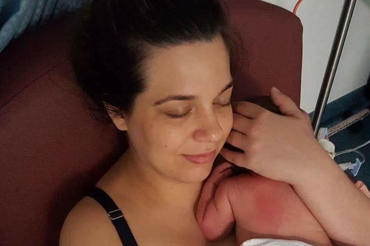 Woman holds her newborn baby to her chest, with her hand cradled around its head.
