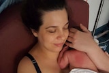 Woman holds her newborn baby to her chest, with her hand cradled around its head.