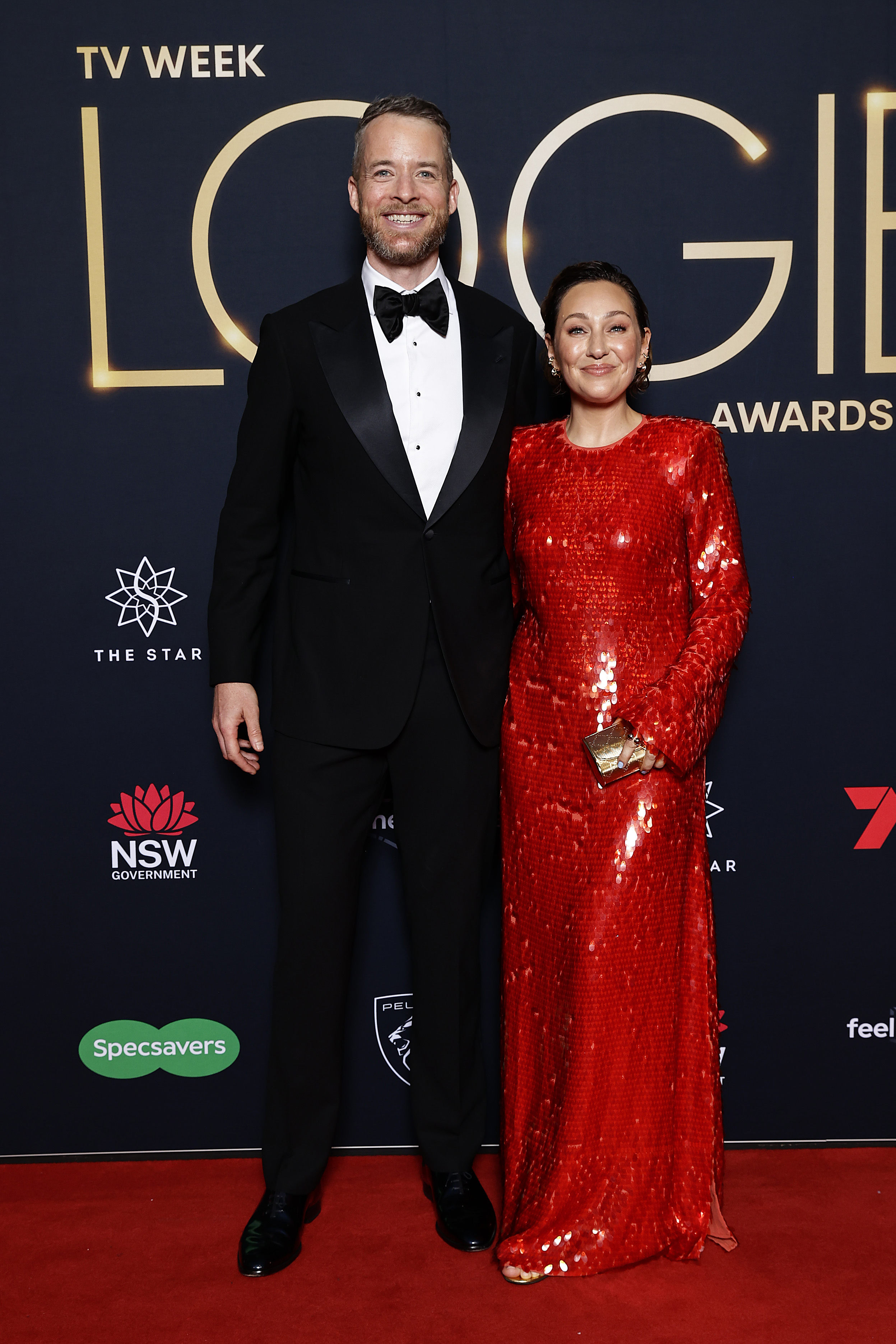 Un hombre y una mujer, un hombre con esmoquin y una mujer con un vestido largo rojo.