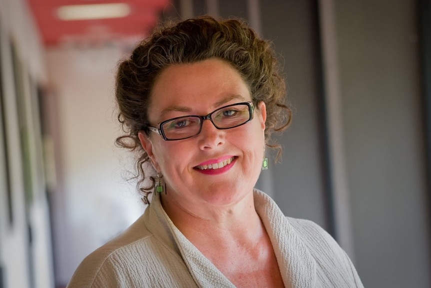 A headshot of a woman with brown curly hair and black glasses.