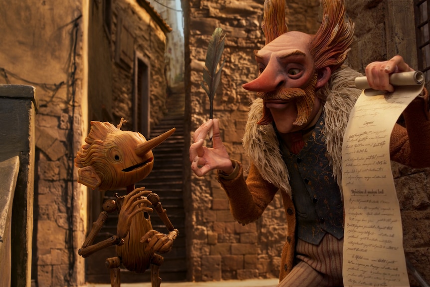 An animated wooden puppet man with a long nose stands in a street with a white man with red spiky hair holding a large parchment