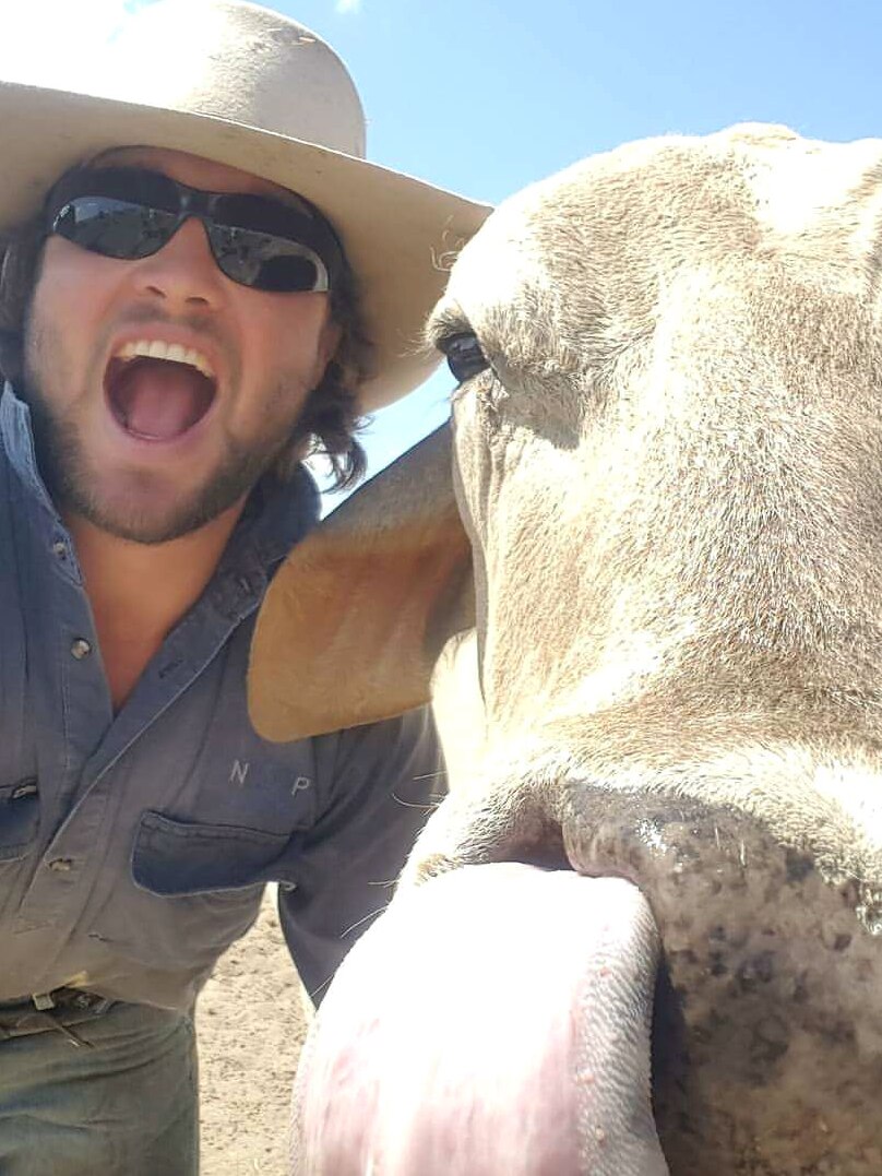 A man with a hat takes a selfie with a cow.