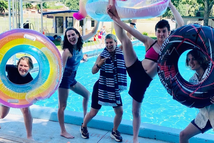 Kids pose with colourful floating devices in front of a pool