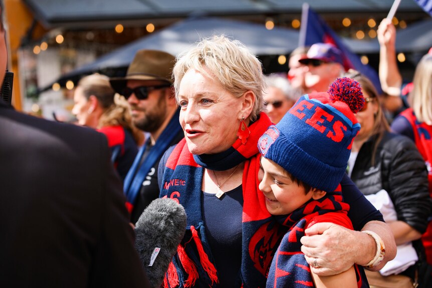 Alannah MacTiernan is interviewed in her Melbourne Demons colours as she hugs a boy