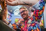 A man wearing a colourful butterfly shirt is cutting a woman's hair in a salon.