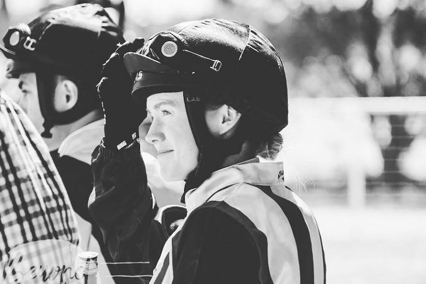 A black and white photo of a woman in a horse riding helmet.