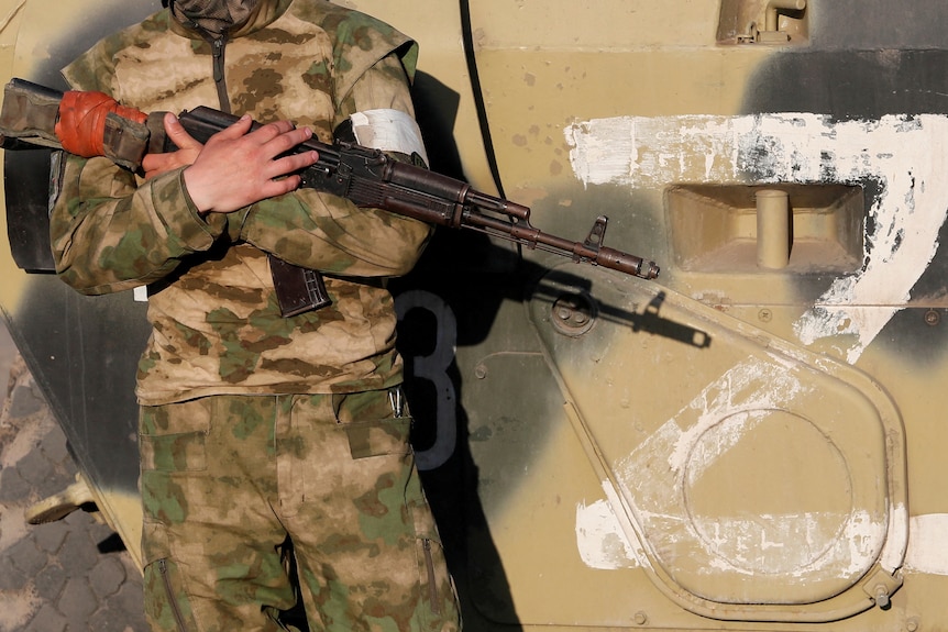 亲俄部队的一名士兵站在一辆带有标志的战车旁边 "z" 他从他身边看着他。
