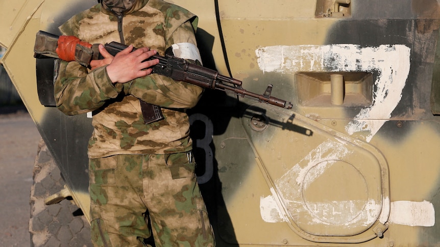 A service member of pro-Russian troops stands guard next to a combat vehicle, with the symbol "Z" seen on its side.