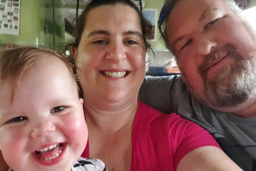 A baby, mum and dad smile at the camera.