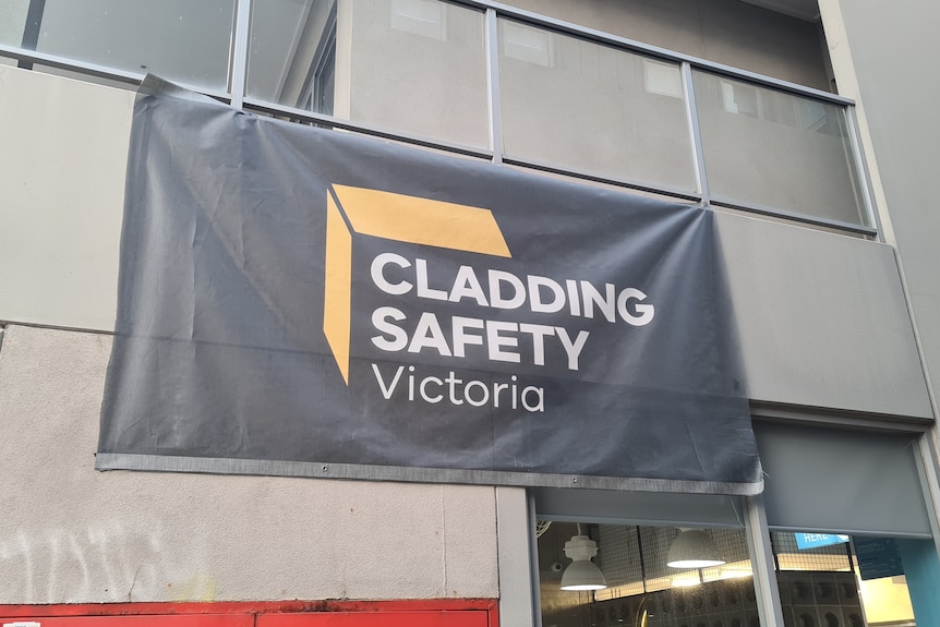A black sign reads 'CLADDING SAFETY VICTORIA', draped on the side of an apartment complex.