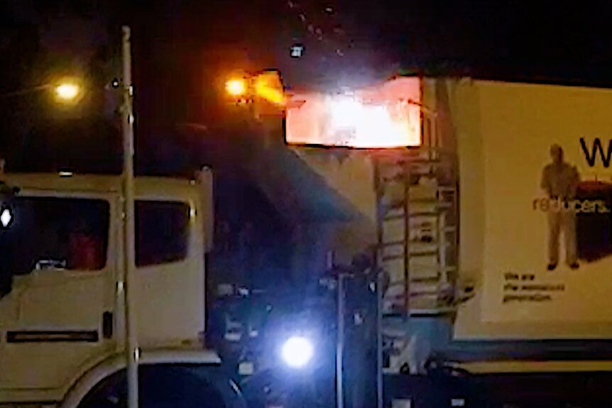 A fire burns inside a garbage truck at night