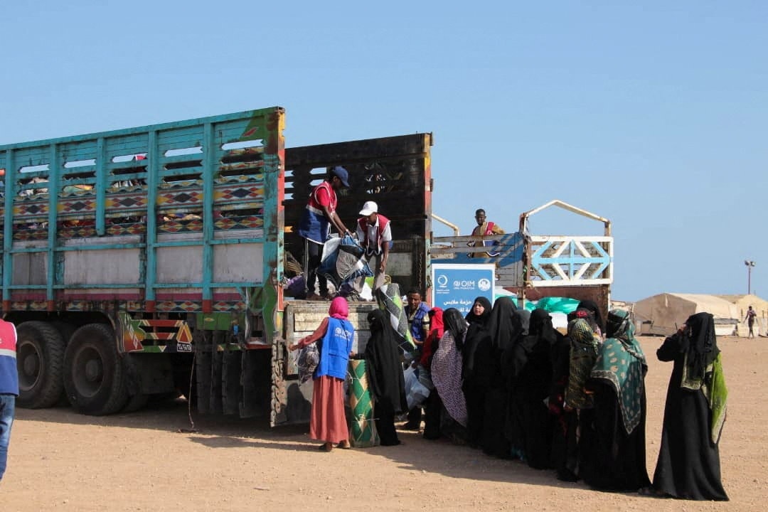 Women dressed in black line up behind a truck waiting for aid.