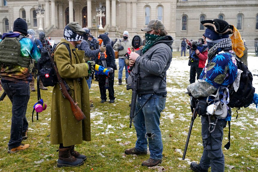 Men with rifles while wearing eclectic outfits including ski masks, pirate hats and Hawaiian shirts.
