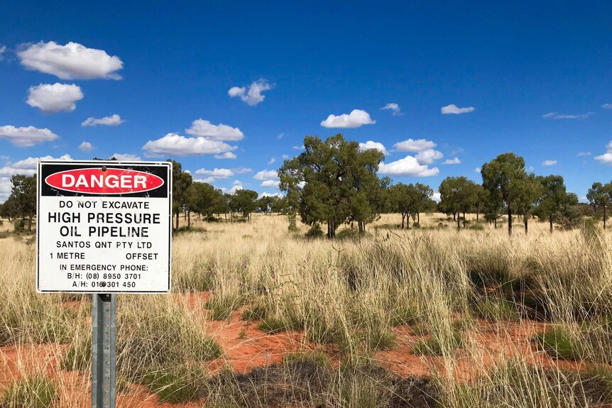 Sign with santos on it in front of red dirt with spinifex.