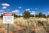 Sign with santos on it in front of red dirt with spinifex.