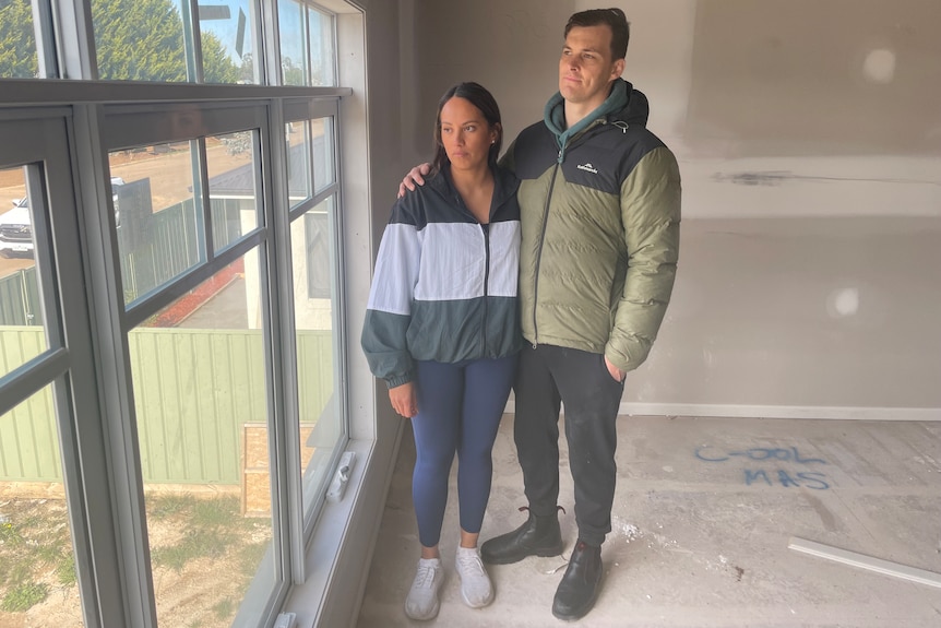 Shontel and Jared Ford stand arm in arm and look out the window on the second story of their partly built home.