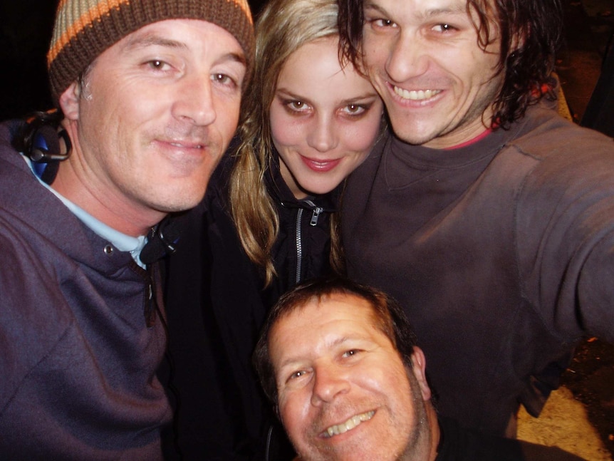 Three men and one woman have their heads in close to smile while posing for a selfie photo.